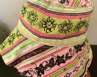 May include: A colorful hat with a brim, featuring a repeating pattern of black floral and sunburst designs on a pink and green striped background. The hat is a mix of white, pink, green, and black.