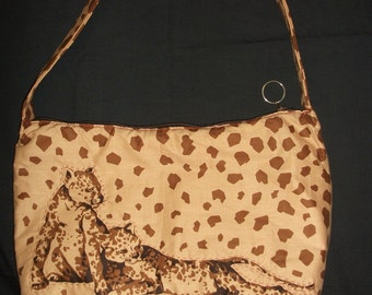 May include: A brown and tan leopard print shoulder bag with a zipper closure. The bag features an embroidered design of two leopards.