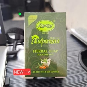 Pode incluir: Uma caixa verde de sabonete de ervas Pyary Malpamara. A caixa apresenta o nome da marca em um oval dourado, com as palavras "Herbal Soap Handmade" abaixo. A caixa também tem uma imagem de um almofariz e pilão com ervas e açafrão. O texto "NEW" é visível.