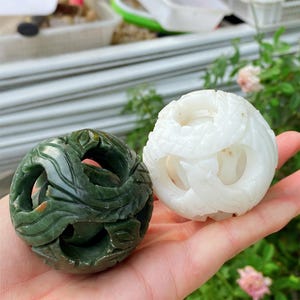 Peut inclure: Deux sphères en pierre sculptée. L'une est vert foncé avec un motif de feuilles, l'autre blanche avec un motif tourbillonnant. Les deux sphères ont des sections ouvertes et sculptées.