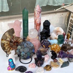 Pode incluir: Uma cole&ccedil;&atilde;o de v&aacute;rios cristais e estatuetas esculpidas. A variedade inclui um obelisco verde, um anjo rosa, uma esfera de quartzo transparente e uma est&aacute;tua de Buda preta. Outros itens incluem uma esfera de labradorita, uma coruja esculpida e v&aacute;rias estatuetas de animais.