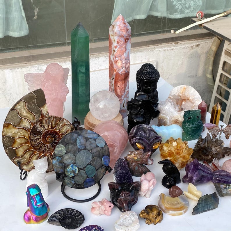 Pode incluir: Uma cole&ccedil;&atilde;o de v&aacute;rios cristais e estatuetas esculpidas. A variedade inclui um obelisco verde, um anjo rosa, uma esfera de quartzo transparente e uma est&aacute;tua de Buda preta. Outros itens incluem uma esfera de labradorita, uma coruja esculpida e v&aacute;rias estatuetas de animais.