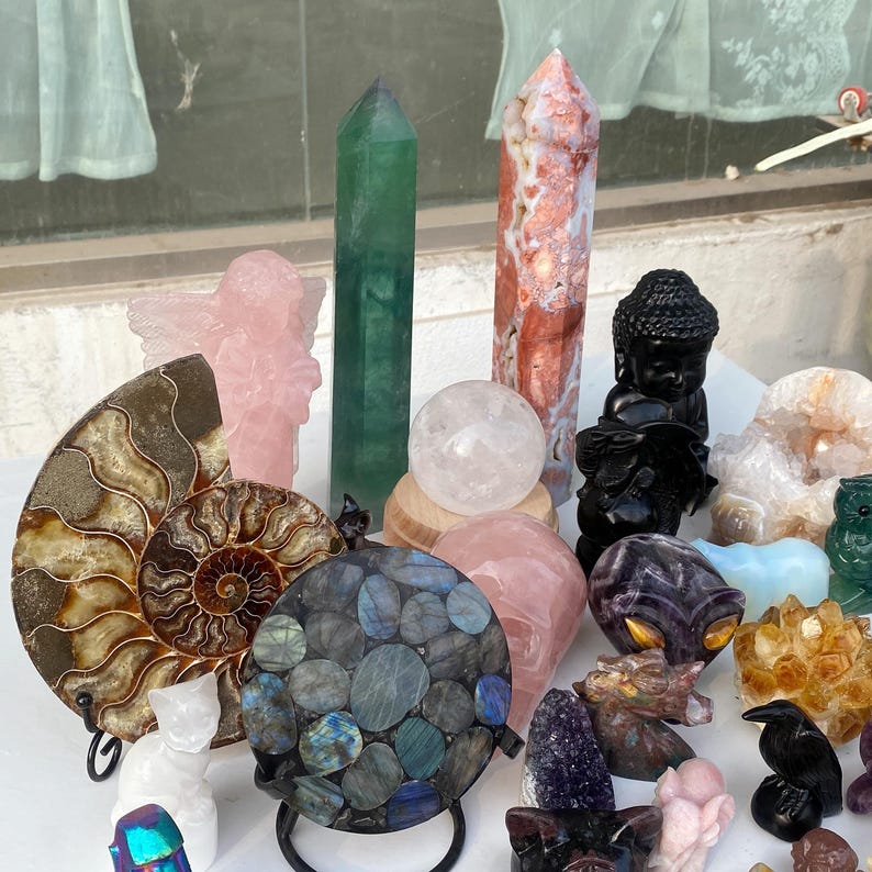 Pode incluir: Uma cole&ccedil;&atilde;o de v&aacute;rios cristais e pedras preciosas. Inclui um obelisco de fluorite verde, um anjo de quartzo rosa, uma est&aacute;tua de Buda preta, uma esfera de quartzo transparente e uma esfera de labradorite. Tamb&eacute;m um corvo esculpido e um f&oacute;ssil de amonite polido.