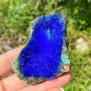 May include: A vibrant blue azurite mineral specimen with a crystalline structure. The azurite is a deep, saturated blue, contrasted by the earthy tones of the surrounding rock matrix. The mineral has a rough, natural texture, with areas of green and brown.