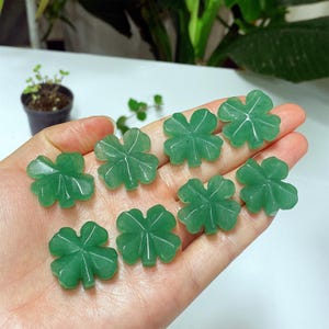 Op de afbeelding: Een verzameling van acht groene, gebeeldhouwde klavers met vier bladeren. Elke klaver heeft een levendige groene kleur, met gedetailleerde adering. De klavers worden gepresenteerd tegen een lichte achtergrond, wat wijst op ambachten of sieraden van natuursteen.