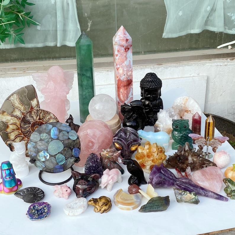 Pode incluir: Uma cole&ccedil;&atilde;o de v&aacute;rios cristais e figuras esculpidas. O sortido inclui um obelisco verde, um anjo rosa, uma est&aacute;tua de Buda preta e uma variedade de figuras de animais, esferas e outras formas em tons de rosa, roxo e transparente.