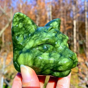 Pode incluir: Uma escultura em pedra verde da cabeça de um gato. A escultura é de um verde vibrante com veios verdes mais escuros, dando-lhe um aspeto natural e texturizado. O olho do gato é detalhado, e a forma geral é lisa e polida.