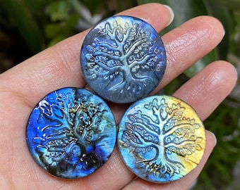 May include: Three round, polished stones with a tree of life design carved into their surfaces. The stones are blue, with hints of yellow and green. The tree carvings are detailed and intricate, with a textured appearance.