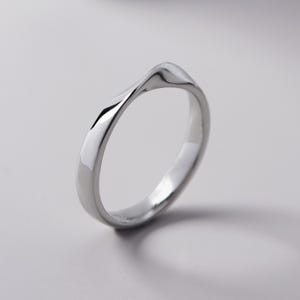 May include: A silver ring with a unique, flowing design. The ring has a smooth, polished surface and a subtle wave pattern. The ring is a simple yet elegant piece of jewelry.