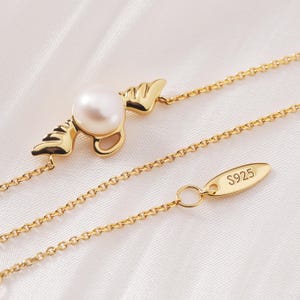 May include: A gold-colored necklace with a pearl pendant. The pendant features a pearl set in a gold-colored design with wing-like accents. The chain is delicate, and the clasp has "S925" stamped on it.