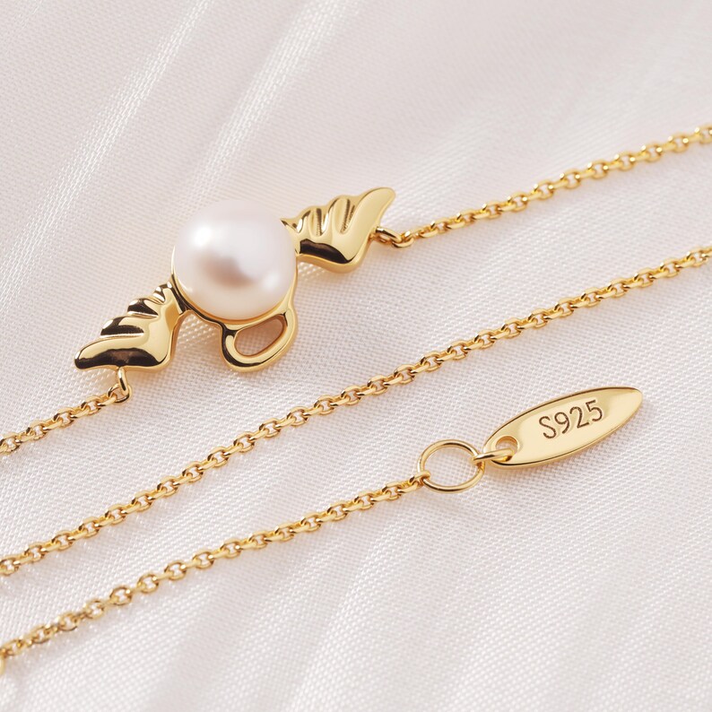 May include: A gold-colored necklace with a pearl pendant. The pendant features a pearl set in a gold-colored design with wing-like accents. The chain is delicate, and the clasp has "S925" stamped on it.