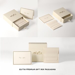 May include: Cream-colored gift boxes and packaging with the "elytis" logo. The boxes are open, revealing a soft interior. Included are small cards with "For you" printed on them, and a small cream-colored pouch.