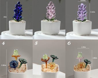 May include: A collection of miniature glass sculptures in white square pots. The sculptures include lavender, flowers, and frogs. The lavender is 4 inches tall. The pots are filled with small white stones. The frog sculptures are 2.8 inches tall.