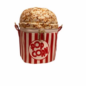 May include: A novelty popcorn-shaped handbag. The top is designed to look like popcorn, while the base is a red and white striped bucket with the words "POP CORN" in a circle. The bag has a zipper closure and small gold handles.