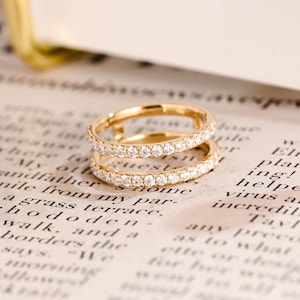 May include: A gold-toned ring featuring a continuous band of small, clear, round-cut stones set along the entire circumference. The metal band has a polished finish, and the stones are arranged in a single row, creating a sparkling, uniform appearance.