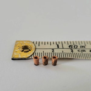 Peut inclure: Trois petits cylindres en céramique brune, chacun d'environ 1,2 cm de long, sont alignés sur une surface blanche à côté d'un ruban à mesurer. Le ruban indique 60 pouces et 3 cm.