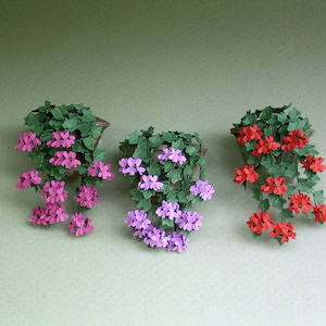 May include: Three hanging flower pots with green leaves and paper flowers. The flowers are pink, purple, and red.