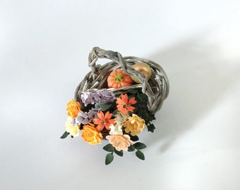 Handmade paper flowers with a pair of scissors an apple and a small pumpkin fill this wicker basket