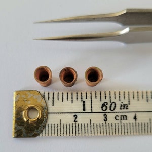May include: Three small, brown, cylindrical objects, possibly ceramic or metal, are lined up on a white surface next to a ruler marked in inches and centimeters. The ruler is 60 inches long.