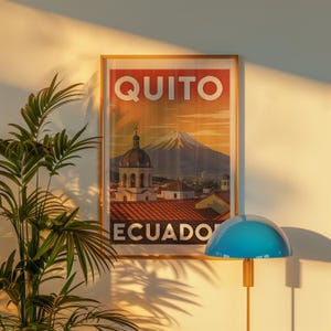 Op de afbeelding: Een ingelijste reisposter met de woorden "QUITO" en "ECUADOR". De poster toont een stadsgezicht met een berg op de achtergrond. Een blauwe lamp met een ronde kap staat op de voorgrond.