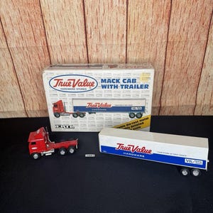 Puede incluir: Un modelo de camión Mack rojo con remolque de True Value Hardware Stores. El modelo es de metal fundido a presión y tiene detalles. El remolque es blanco con la marca True Value en azul y rojo.