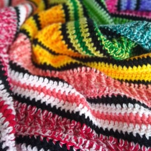 May include: A colorful, handmade crochet blanket. The blanket features a vibrant mix of colors including red, pink, yellow, green, and blue. The crochet pattern includes black stripes that separate the different color sections.