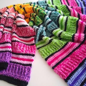 May include: A colorful, handmade crochet blanket with a striped pattern. The blanket features a vibrant array of colors, including pink, purple, green, yellow, and blue, with black stripes separating the color blocks. The blanket is folded and draped.