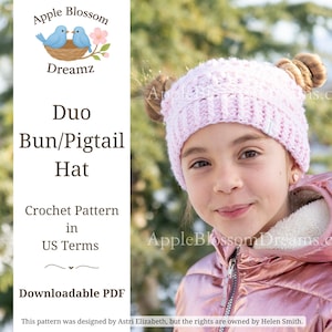 May include: A young person wearing a light pink crocheted hat with two bun-style accents. The hat is part of a crochet pattern labeled "Duo Bun/Pigtail Hat" in US terms. The image includes the text "Apple Blossom Dreamz" and "Downloadable PDF".