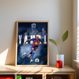 K&ouml;nnte beinhalten: Gerahmter Druck mit einem Fu&szlig;ballspieler in blau-roter Uniform, der einen Fu&szlig;ball tritt. Das Wort "YAMAL" wird in gro&szlig;en wei&szlig;en Buchstaben angezeigt. Der Hintergrund zeigt ein verschwommenes Bild desselben Spielers.