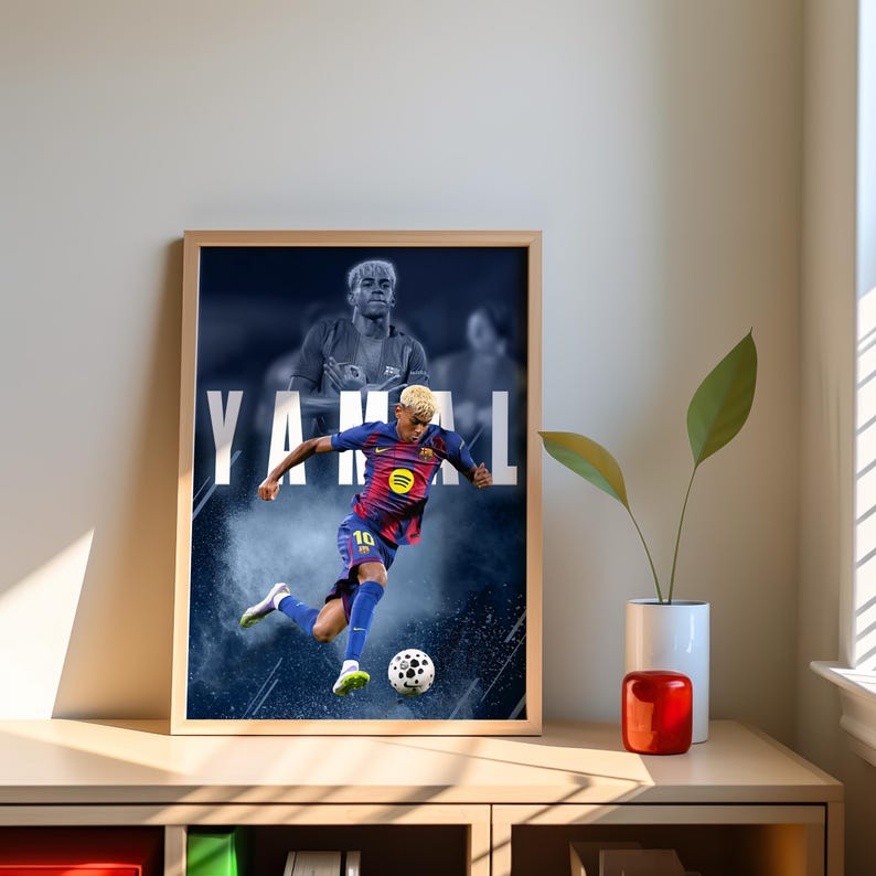 K&ouml;nnte beinhalten: Gerahmter Druck mit einem Fu&szlig;ballspieler in blau-roter Uniform, der einen Fu&szlig;ball tritt. Das Wort "YAMAL" wird in gro&szlig;en wei&szlig;en Buchstaben angezeigt. Der Hintergrund zeigt ein verschwommenes Bild desselben Spielers.