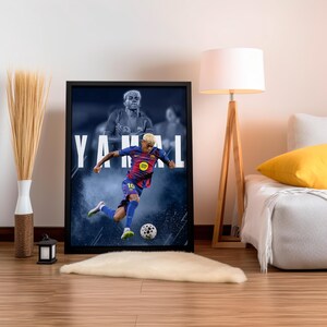 K&ouml;nnte beinhalten: Gerahmtes Poster mit einem Fu&szlig;ballspieler in blau-roter Uniform, der einen Fu&szlig;ball tritt. Der Name des Spielers, YAMAL, ist in gro&szlig;en wei&szlig;en Buchstaben dargestellt. Der Hintergrund zeigt ein verschwommenes Bild des Spielers.