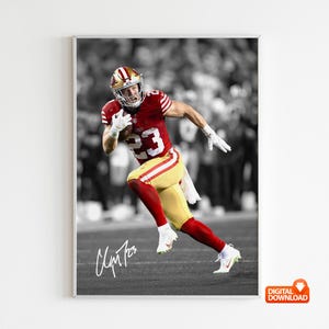 May include: A framed digital print of a football player in a red and gold uniform, number 23, running with the ball. The background is in black and white, with the player in full color. The player's signature is at the bottom.