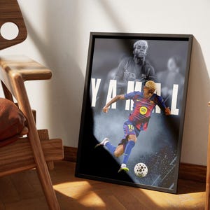 K&ouml;nnte beinhalten: Ein gerahmtes Poster mit einem Fu&szlig;ballspieler in einem blau-roten Trikot, der einen Ball tritt. Auf dem Poster steht der Name "YAMAL" in gro&szlig;en wei&szlig;en Buchstaben. Das Bild ist in einem schwarzen Rahmen, mit einem verschwommenen Bild des Spielers im Hintergrund.