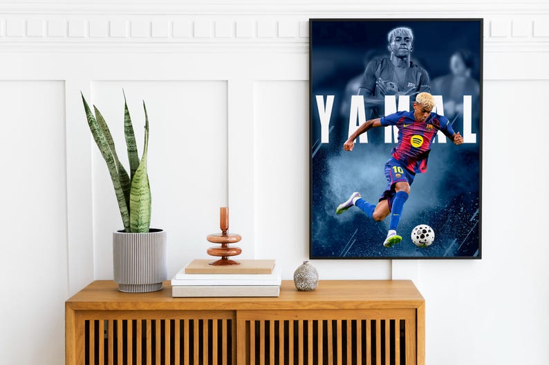 K&ouml;nnte beinhalten: Ein gerahmtes Poster mit einem Fu&szlig;ballspieler in blau-roter Uniform, der einen Ball tritt. Der Name des Spielers, YAMAL, ist in gro&szlig;en wei&szlig;en Buchstaben dargestellt. Das Poster h&auml;ngt &uuml;ber einem Holzschrank mit einer Pflanze und Dekoration.