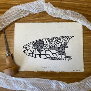 May include: Black and white line art print of a gopher snake head on a cream colored paper. The print is titled "Gopher Snake" and signed "KS 2023".