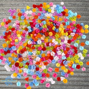 Puede incluir: Un vibrante surtido de botones coloridos en varias formas, incluyendo círculos, cuadrados, triángulos y lazos. Los botones son en tonos de rojo, naranja, amarillo, verde, azul, rosa y morado. Estos pequeños botones decorativos son ideales para manualidades y costura.