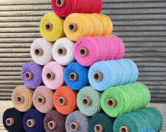 Könnte beinhalten: Eine Pyramide aus farbenfrohen Garnrollen in verschiedenen Farbtönen, darunter Rot, Gelb, Rosa, Blau und Grün. Jede Rolle ist zylindrisch mit einem zentralen Holzkern. Das Garn scheint aus Baumwolle oder einer ähnlichen Faser zu bestehen.