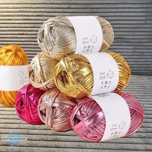 Puede incluir: Un conjunto de madejas de hilo metálico en oro, plata y rosa. Cada madeja está envuelta con una etiqueta blanca. El hilo tiene una superficie brillante y reflectante, ideal para proyectos de manualidades.