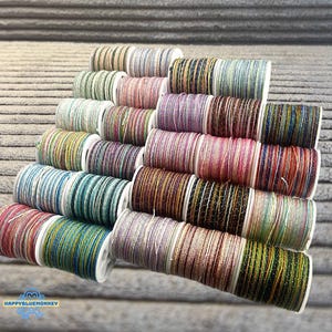 May include: A collection of colorful spools of thread, each wound with a different color of metallic thread. The spools are arranged in a tiered display, showcasing a variety of colors including pink, blue, green, and gold. The thread appears to be for crafting or embroidery.