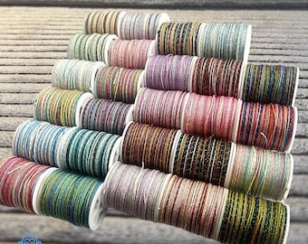 May include: A collection of colorful spools of thread, each wound with a different color of metallic thread. The spools are arranged in a tiered display, showcasing a variety of colors including pink, blue, green, and gold. The thread appears to be for crafting or embroidery.