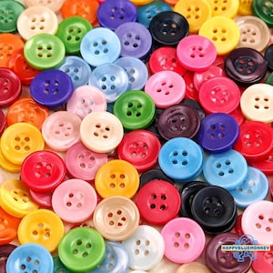 May include: A collection of colorful round buttons in various shades, including red, yellow, green, blue, purple, pink, and black. Each button has four holes for sewing and a slightly raised edge.