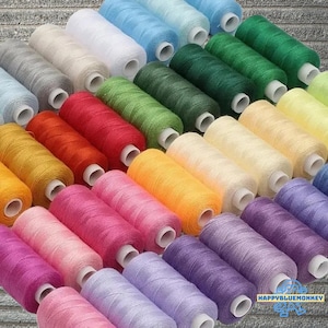 Peut inclure: Une collection de bobines de fil colorées dans diverses nuances, notamment le bleu, le vert, le jaune, le rose et le violet. Les bobines sont soigneusement disposées, présentant un spectre de couleurs pour les projets de couture et d'artisanat.