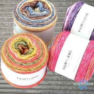 Peut inclure: Trois écheveaux de fil colorés. L'un est un mélange de jaune, d'orange et de vert. Un autre est un mélange de bleu, de marron et de beige. Le troisième est rose et violet. Chaque écheveau porte une étiquette blanche avec le mot "FAIRYLAND".