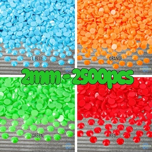 May include: A collection of 2500 pieces of 2mm round flat-back rhinestones in four distinct colours. The image displays sections labelled L BLUE, ORANGE, GREEN, and RED, each featuring a dense pile of small, circular, vibrant coloured gems.