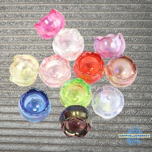 May include: A collection of eleven translucent, flower-shaped beads in various colors including pink, yellow, red, green, blue, and clear. Each bead features a central hole and a petal-like design. The text HAPPYBLUEMONKEY is visible.