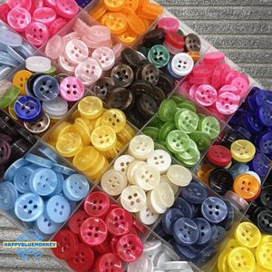 May include: A variety of colorful buttons in a clear divided container. The buttons are in shades of pink, orange, yellow, green, blue, white, and black. The buttons are round with four holes. The text "HAPPYBLUEMONKEY" is visible in the lower left corner.
