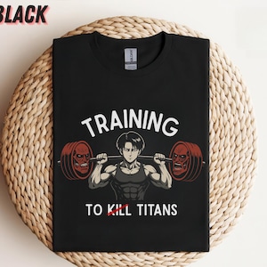 K&ouml;nnte beinhalten: Schwarzes T-Shirt mit dem Text "TRAINING TO KILL TITANS" und einer Grafik eines muskul&ouml;sen Anime-Charakters, der eine Langhantel mit zwei roten, monstergesichtigen Gewichten hebt. Das Wort "BLACK" befindet sich oben links.