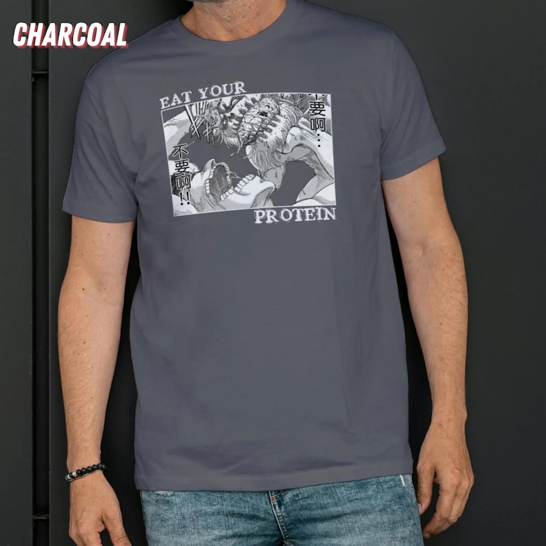 May include: Charcoal gray t-shirt featuring a manga-style graphic with the words "EAT YOUR PROTEIN". The graphic depicts a stylized battle scene with Japanese text. The shirt is a crew neck and short-sleeved.