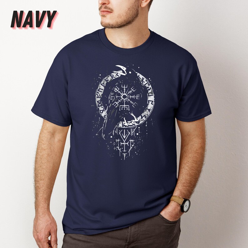 K&ouml;nnte beinhalten: Marineblaues T-Shirt mit einer wei&szlig;en Raben-Grafik in einem kreisf&ouml;rmigen Runen-Design. Das Wort "NAVY" ist in Rosa oben links aufgedruckt. Das T-Shirt hat kurze &Auml;rmel und einen Rundhalsausschnitt.