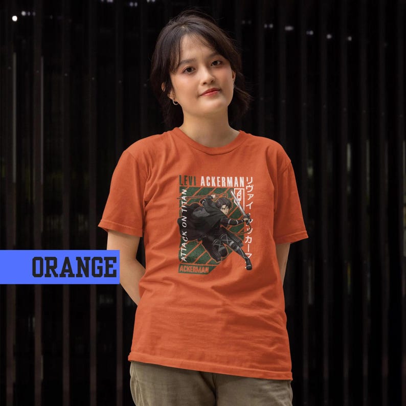 May include: Orange t-shirt featuring a graphic of a character with a sword, with text that reads "Levi Ackerman" and "Attack on Titan" in English and Japanese. The shirt is a solid orange color.